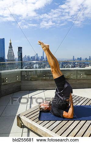 Stock Image - Caucasian man with legs raised performing yoga on urban rooftop. Fotosearch