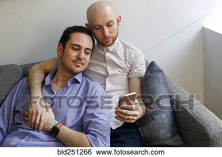 Stock Photograph - Caucasian men holding hands and texting on cell phone. Fotosearch