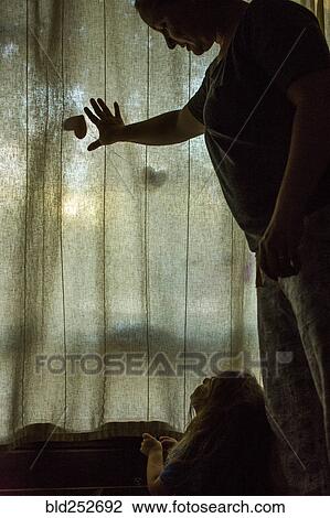 Stock Image - Caucasian mother and daughter looking at window curtain. Fotosearch