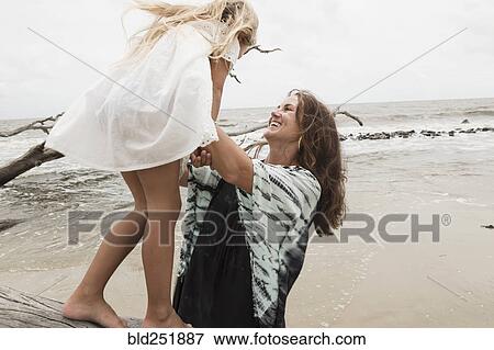 Stock Photo - Caucasian mother and daughter playing on driftwood on beach. Fotosearch