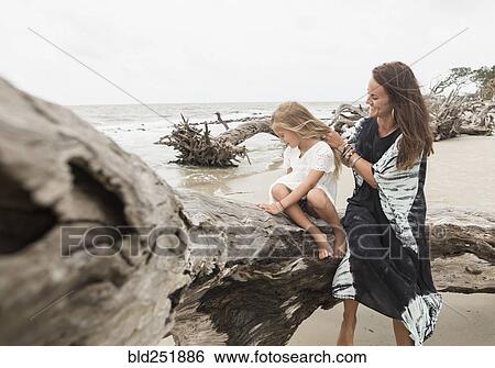 Caucasian mother and daughter sitting on driftwood on beach View Large Photo Image Stock Photograph - Caucasian mother and daughter sitting on driftwood on beach. Fotosearch