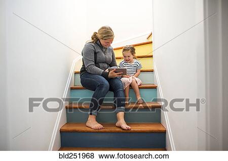 Stock Photo - Caucasian mother and daughter using digital tablet on staircase. Fotosearch