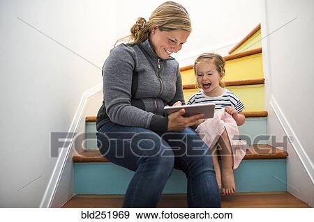 Stock Photo - Caucasian mother and daughter using digital tablet on staircase. Fotosearch