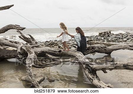 Stock Photo - Caucasian mother and daughter walking on driftwood on beach. Fotosearch