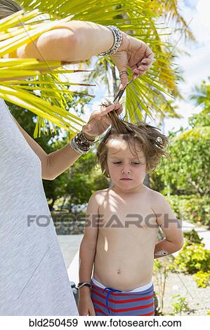 Stock Photo - Caucasian mother cutting hair of son outdoors. Fotosearch
