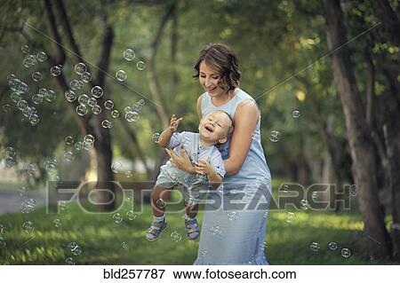 Caucasian mother holding baby son playing with bubbles View Large Photo Image Stock Photo - Caucasian mother holding baby son playing with bubbles. Fotosearch