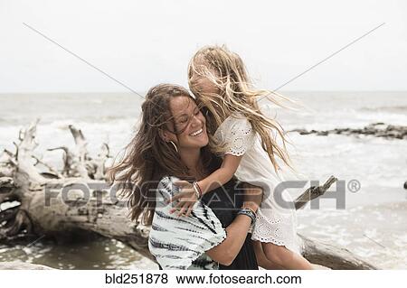 Stock Photo - Caucasian mother hugging daughter near driftwood on beach. Fotosearch