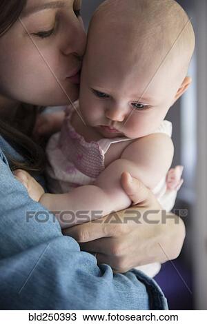 Stock Image - Caucasian mother kissing cheek of baby daughter. Fotosearch