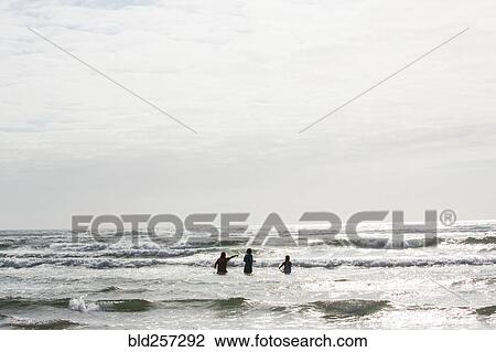 Stock Image - Caucasian people wading in ocean waves. Fotosearch