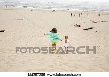 Stock Photography - Caucasian sisters holding hands and running on beach. Fotosearch