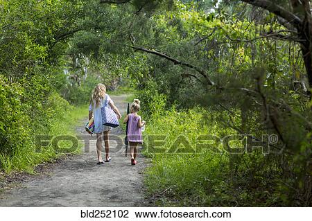 Stock Image - Caucasian sisters walking on dirt path. Fotosearch