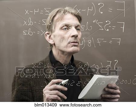 Stock Photo - Caucasian teacher looking at formula on glass wall. Fotosearch