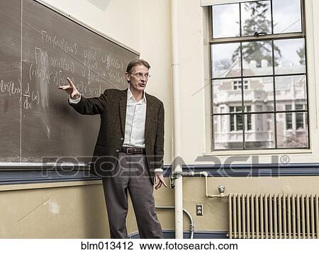 Stock Image - Caucasian teacher writing on blackboard. Fotosearch