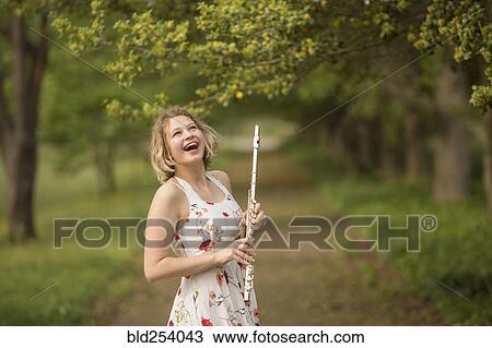 Stock Image - Caucasian teenage girl holding flute in park and laughing. Fotosearch