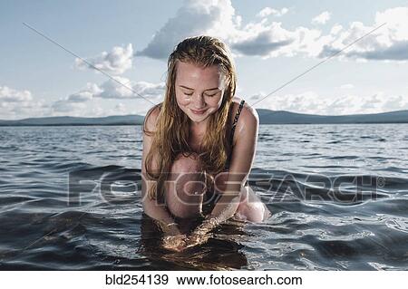 Stock Photo - Caucasian teenage girl kneeling in ocean. Fotosearch