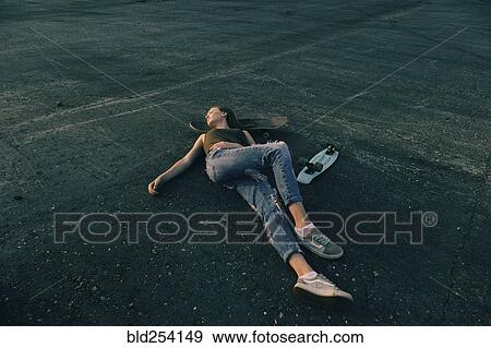 Caucasian teenage girl laying on pavement with head on skateboard View Large Photo Image Stock Photo - Caucasian teenage girl laying on pavement with head on skateboard. Fotosearch