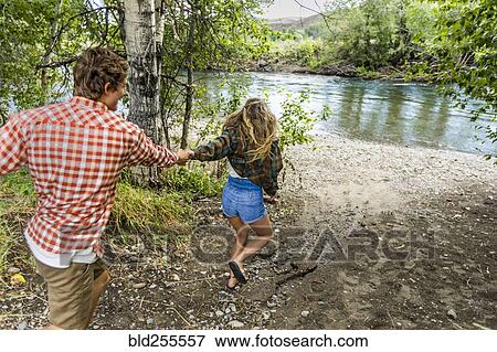 Stock Photo - Caucasian teenage girl leading boy to river. Fotosearch