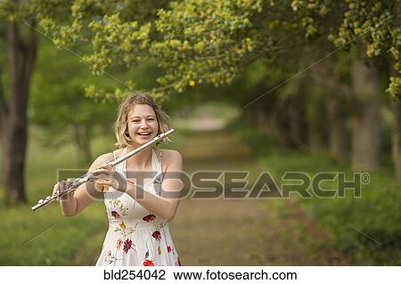 Stock Image - Caucasian teenage girl playing flute in park. Fotosearch