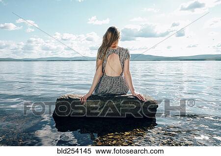 Stock Photography - Caucasian teenage girl sitting on rock in ocean. Fotosearch