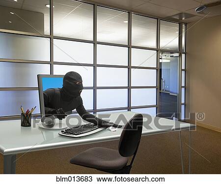 Stock Image - Caucasian thief coming out of computer monitor in office. Fotosearch