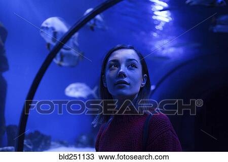 Stock Image - Caucasian woman admiring fish in aquarium. Fotosearch