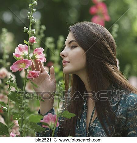 Stock Image - Caucasian woman admiring pink flowers. Fotosearch