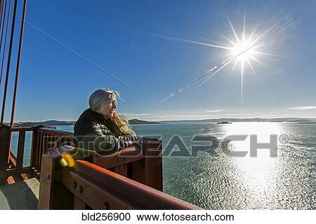Stock Image - Caucasian woman admiring scenic view on bridge. Fotosearch