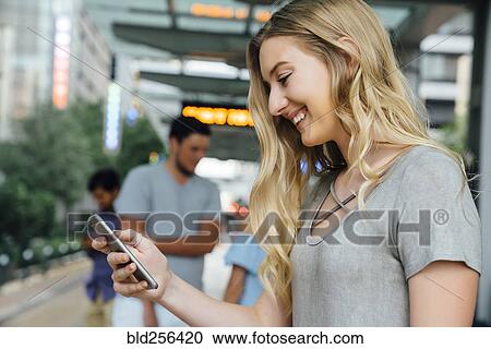 Stock Image - Caucasian woman at train station texting on cell phone. Fotosearch