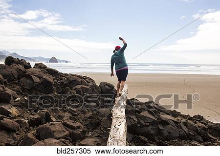 Stock Photography - Caucasian woman balancing on log on rocks at beach. Fotosearch