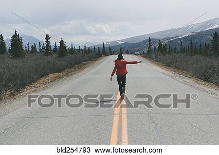 Stock Image - Caucasian woman balancing on stripes in two-lane road. Fotosearch