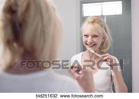 Stock Image - Caucasian woman brushing teeth in mirror. Fotosearch
