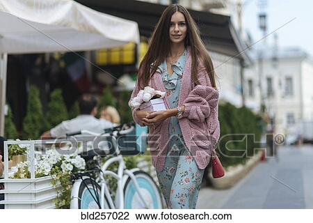 Stock Image - Caucasian woman carrying gift box near bicycle. Fotosearch
