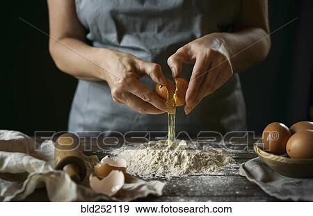 Stock Photo - Caucasian woman cracking egg over flour. Fotosearch