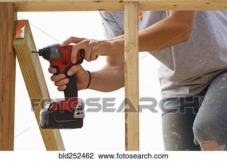 Stock Image - Caucasian woman drilling lumber at construction site. Fotosearch