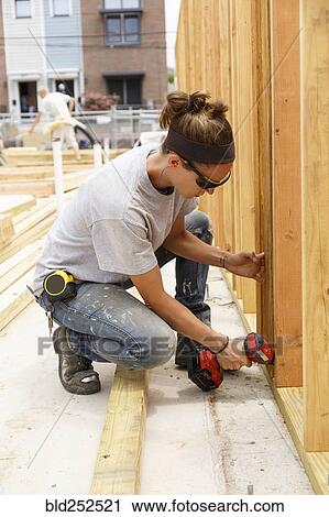 Stock Image - Caucasian woman drilling lumber at construction site. Fotosearch