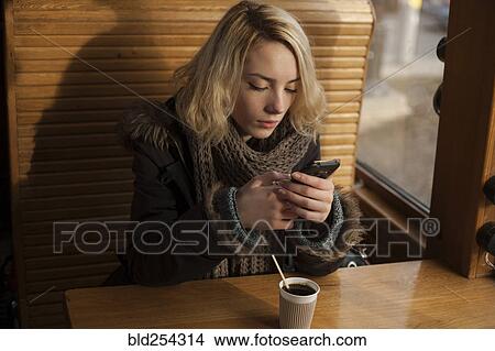 Picture - Caucasian woman drinking coffee and texting on cell phone. Fotosearch