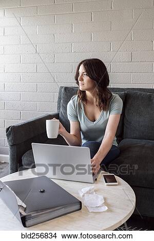 Picture - Caucasian woman drinking coffee and using laptop. Fotosearch