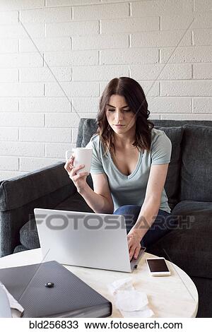 Stock Image - Caucasian woman drinking coffee and using laptop. Fotosearch