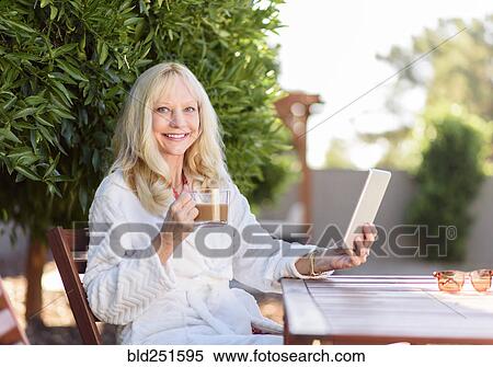 Stock Photography - Caucasian woman drinking coffee and using digital tablet. Fotosearch