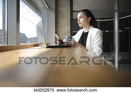 Stock Photography - Caucasian woman drinking coffee and texting on cell phone. Fotosearch