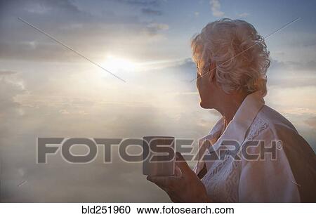 Stock Image - Caucasian woman drinking coffee admiring cloudy sky. Fotosearch
