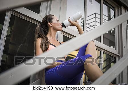 Stock Image - Caucasian woman drinking water on urban staircase. Fotosearch