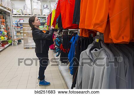 Stock Image - Caucasian woman examining shirt in store. Fotosearch