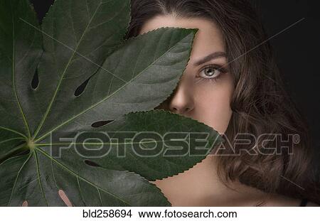 Picture - Caucasian woman hiding behind green leaf. Fotosearch