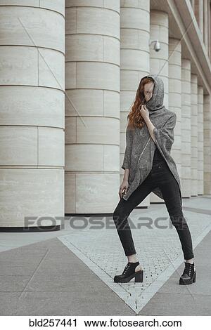 Stock Image - Caucasian woman hiding face behind hood near pillars. Fotosearch