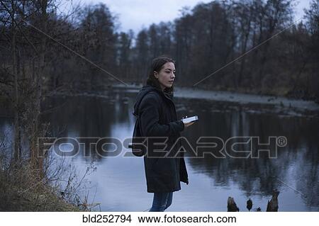 Picture - Caucasian woman holding cell phone near river. Fotosearch