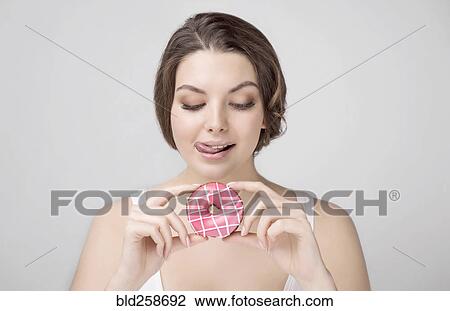 Stock Image - Caucasian woman holding donut and licking lips. Fotosearch