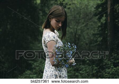 Stock Image - Caucasian woman holding flowers in forest. Fotosearch