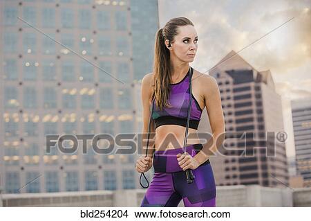 Picture - Caucasian woman holding jump rope on urban rooftop. Fotosearch