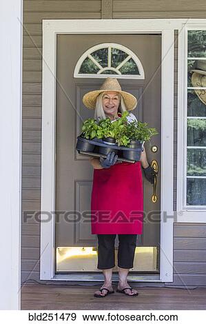 Stock Photo - Caucasian woman holding potted plants in doorway. Fotosearch